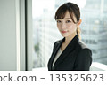 Portrait of a young Japanese woman looking at camera while standing by a window in an office 135325623