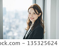 Portrait of a young Japanese woman looking at camera while standing by a window in an office 135325624