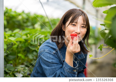 A woman holding a strawberry with a smile 135326308