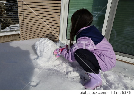 Girl making a snowman, enjoying winter moments in front of her house Girl making a snowman, enjoying winter moments in front of her house 135326376