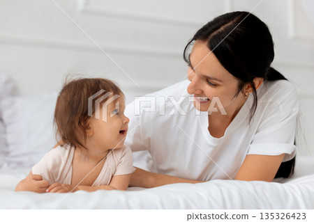 Mother and infant baby lying together on bed at home and smiling 135326423