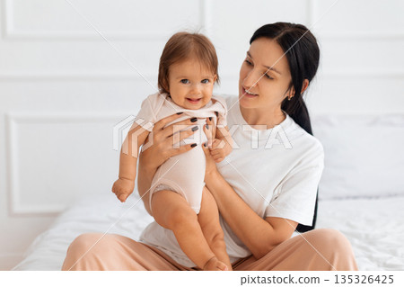 Happy baby smiling while being held by mother on bed Happy baby smiling while being held by mother on bed 135326425