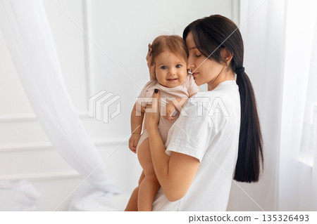 Mother holding her infant baby at home in bright minimalist interior 135326493