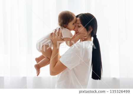 Mother kissing her infant baby at home in a soft light interior 135326499