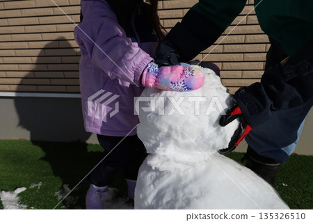 Parents and children build snowmen and spend warm moments working together in the winter garden 135326510