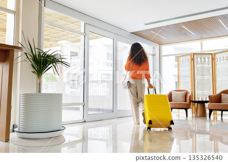 Adult caucasian woman walking away in hotel lobby with yellow suitcase Adult caucasian woman walking away in hotel lobby with yellow suitcase 135326540