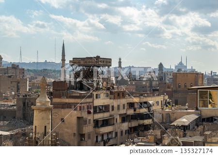 A panoramic view of Old Cairo in Egypt showcases historic buildings, minarets, and rooftops under a cloudy sky. The scene reflects the rich architectural heritage of the city. 135327174