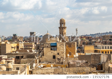 A panoramic view of Old Cairo in Egypt showcases historic buildings, minarets, and rooftops under a cloudy sky. The scene reflects the rich architectural heritage of the city. A panoramic view of Old Cairo in Egypt showcases historic buildings, minarets, and rooftops under a cloudy sky. The scene reflects the rich architectural heritage of the city. 135327176