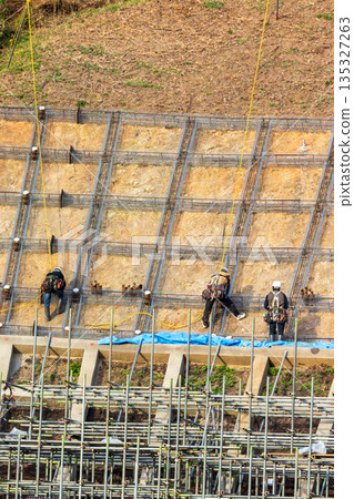 Workers securing slopes while attached to ropes for safety 135327263