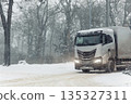 Winter logistics scene cargo truck driving heavy snowfall icy road forest city suburban urban landscape low visibility conditions. Scenic freight transport cold weather risk supply chain challenge 135327311