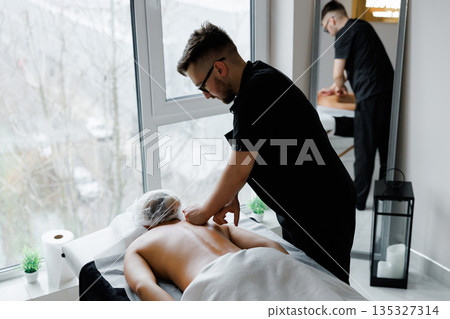 Male therapist massaging woman's back during wellness treatment Male therapist massaging woman's back during wellness treatment 135327314