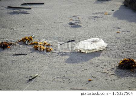 Abandoned plastic container on beach sand illustrating irresponsible waste disposal and sustainability challenges 135327504