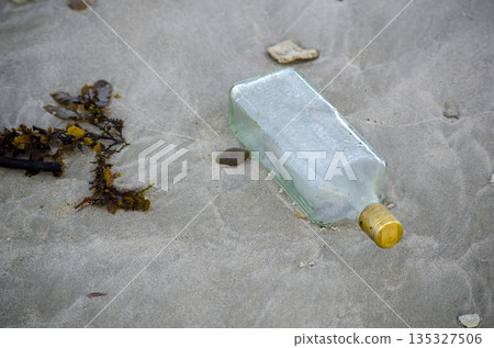 Discarded glass bottle lying on wet sand surface symbolizing urban litter pollution and careless waste disposal 135327506