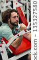 A focused workout session in vertical photo of a Caucasian man targets his biceps on a Scott bench press, showcasing determination and muscular control. Gym workout. Bicep exercise. 135327580