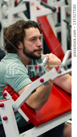 A focused workout session in vertical photo of a Caucasian man targets his biceps on a Scott bench press, showcasing determination and muscular control. Gym workout. Bicep exercise. A focused workout session in vertical photo of a Caucasian man targets his biceps on a Scott bench press, showcasing determination and muscular control. Gym workout. Bicep exercise. 135327580