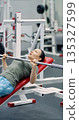 Gym workout. Photo of a middle-aged woman pushes through a bench press set on the hammer machine, combining steady breathing and firm control for an effective workout. 135327599