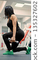 Middle aged fitness woman lunging with dumbbells in gym. Controlled dumbbell lunges help the middle-aged woman develop muscle tone and endurance. Close-up vertical photo. 135327602