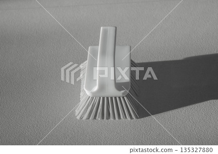 A white floor cleaning brush is lying on the floor. A white floor cleaning brush is lying on the floor. 135327880