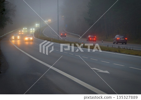 Car traveling on the foggy road with headlights or headlamps on. Low visibility Dangerous driving of cars in winter in bad weather Car traveling on the foggy road with headlights or headlamps on. Low visibility Dangerous driving of cars in winter in bad weather 135327889