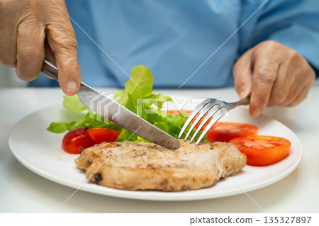 Asian elderly woman patient eating pork chop stake and vegetable salad for healthy food in hospital. Asian elderly woman patient eating pork chop stake and vegetable salad for healthy food in hospital. 135327897