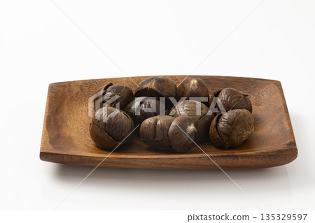 Roasted chestnuts on a wooden plate_white background Roasted chestnuts on a wooden plate_white background 135329597