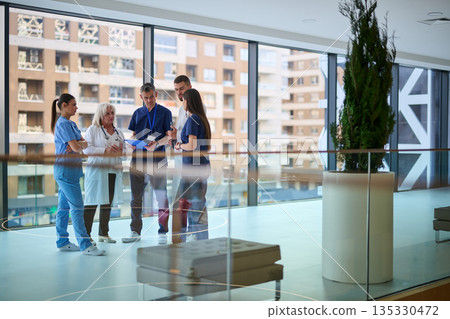 Team of healthcare professionals discussing patient care in a modern hospital setting during the daytime 135330472