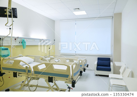 Modern hospital room with multiple patient beds and seating area during daytime Modern hospital room with multiple patient beds and seating area during daytime 135330474