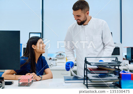 Male lab technician assists female colleague in modern laboratory while discussing research data during work hours 135330475