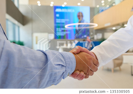 Business professionals engage in a handshake inside a modern office lobby during a meeting in the afternoon Business professionals engage in a handshake inside a modern office lobby during a meeting in the afternoon 135330505