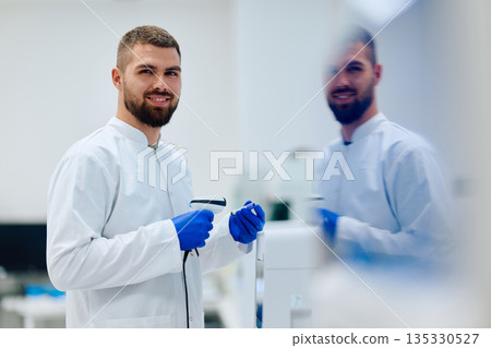Young scientist in lab coat holds equipment and smiles in modern laboratory setting during work hours 135330527