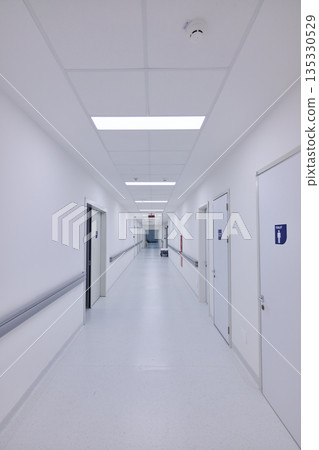 Long, bright hospital corridor with clean white walls and doors leading to patient rooms 135330529
