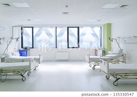 Modern hospital room with several empty patient beds and large windows during daytime 135330547