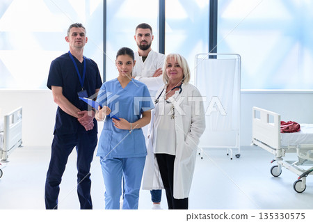 Healthcare professionals stand together in a bright hospital setting while a patient is treated in the background Healthcare professionals stand together in a bright hospital setting while a patient is treated in the background 135330575