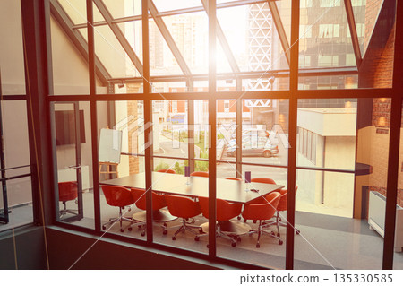 Modern conference room with orange chairs and large windows in a city building during sunset Modern conference room with orange chairs and large windows in a city building during sunset 135330585