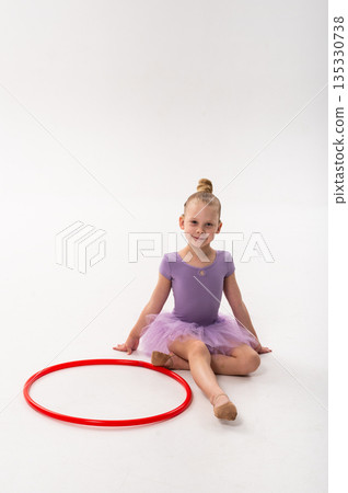 Young dancer with a cochlear implant sits beside a red hoop after ballet practice. Inclusive performance, hearing support, and calm childhood confidence through rhythmic dance and movement. Young dancer with a cochlear implant sits beside a red hoop after ballet practice. Inclusive performance, hearing support, and calm childhood confidence through rhythmic dance and movement. 135330738