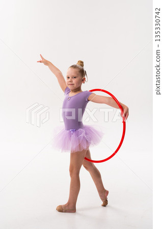 Young dancer with a cochlear implant balances with a red hoop during studio training. Inclusive performance, auditory support, and physical development through rhythmic gymnastics and ballet. Young dancer with a cochlear implant balances with a red hoop during studio training. Inclusive performance, auditory support, and physical development through rhythmic gymnastics and ballet. 135330742