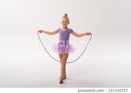 Smiling ballerina with a cochlear implant poses with a rope in a lavender tutu. Inclusive ballet, hearing technology, and confident childhood expression through rhythmic gymnastics and dance. Smiling ballerina with a cochlear implant poses with a rope in a lavender tutu. Inclusive ballet, hearing technology, and confident childhood expression through rhythmic gymnastics and dance. 135330757