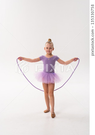 Young ballerina with a cochlear implant stretches a red hoop while posing in a lavender tutu. Inclusive gymnastics, hearing technology, and childhood coordination through rhythmic dance and movement. 135330758