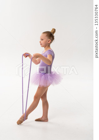 Young dancer with a cochlear implant holds a rope in profile during ballet training. Inclusive movement, auditory support, and physical development through rhythmic gymnastics and dance practice. Young dancer with a cochlear implant holds a rope in profile during ballet training. Inclusive movement, auditory support, and physical development through rhythmic gymnastics and dance practice. 135330764