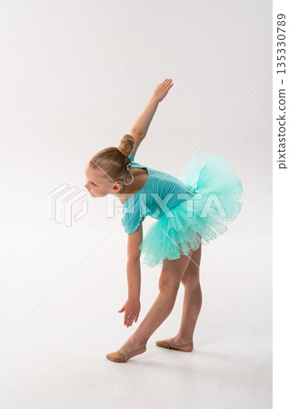 Young dancer with a cochlear implant bends forward in a turquoise ballet costume. Adaptive performance, hearing technology, and physical coordination through classical dance and therapy. 135330789