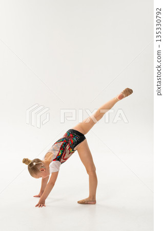 Young gymnast with a cochlear implant performs a forward split balance on the floor. Rehabilitation, auditory technology, and physical development through rhythmic gymnastics and inclusive dance 135330792