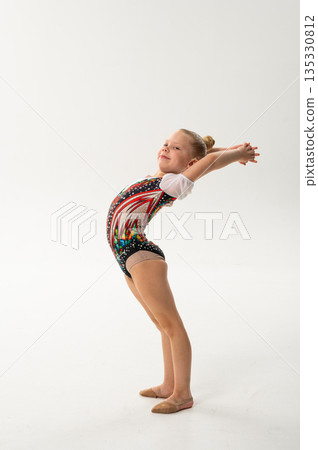 Young rhythmic gymnast with cochlear implant posing in training leotard in studio. Hearing rehabilitation, inclusive childhood sport and body awareness through flexibility and balance 135330812