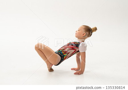 Young rhythmic gymnast with cochlear implant posing in training leotard in studio. Hearing rehabilitation, inclusive childhood sport and body awareness through flexibility and balance 135330814