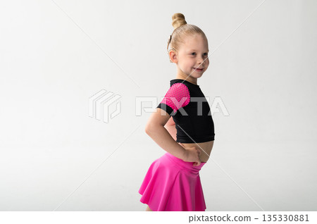 Smiling dancer with cochlear implant posing in pink costume in studio. Copy space. Pediatric hearing support, inclusive sport and childhood confidence through expressive dance movement 135330881