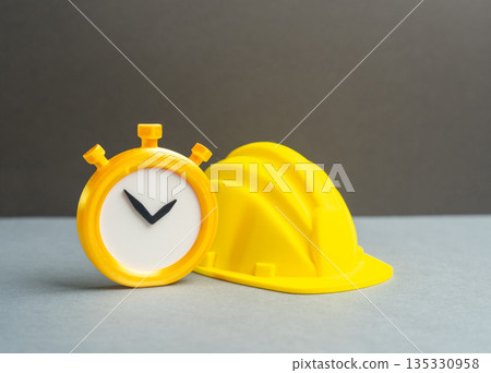 A stopwatch and a yellow construction hard hat. Temporary part-time work, seasonal work. Overtime. Flexible labor, time tracking and workforce intensity in construction. A stopwatch and a yellow construction hard hat. Temporary part-time work, seasonal work. Overtime. Flexible labor, time tracking and workforce intensity in construction. 135330958