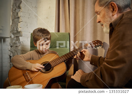 Senior mentor showing guitar chords to young boy at home. Senior mentor showing guitar chords to young boy at home. 135331027
