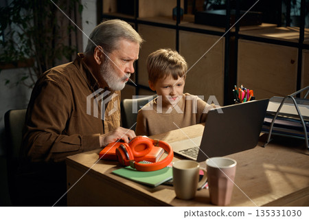 Young boy mentoring senior man using laptop at home desk. 135331030