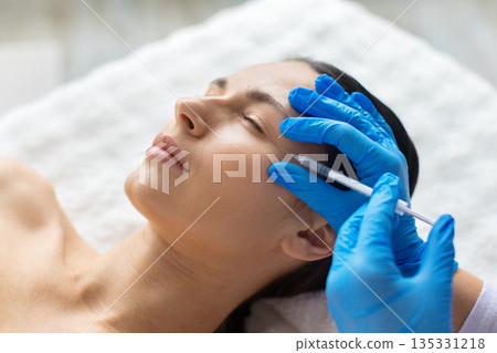 Closeup of young beautiful woman undergoing professional aesthetic facial procedure with syringe 135331218