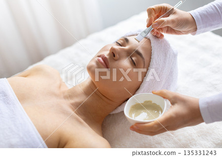 Young caucasian woman lying peacefully while facial mask is applied at spa 135331243