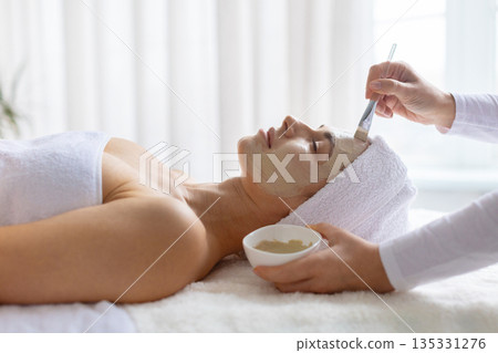 Woman enjoying facial clay mask treatment at spa, eyes closed 135331276